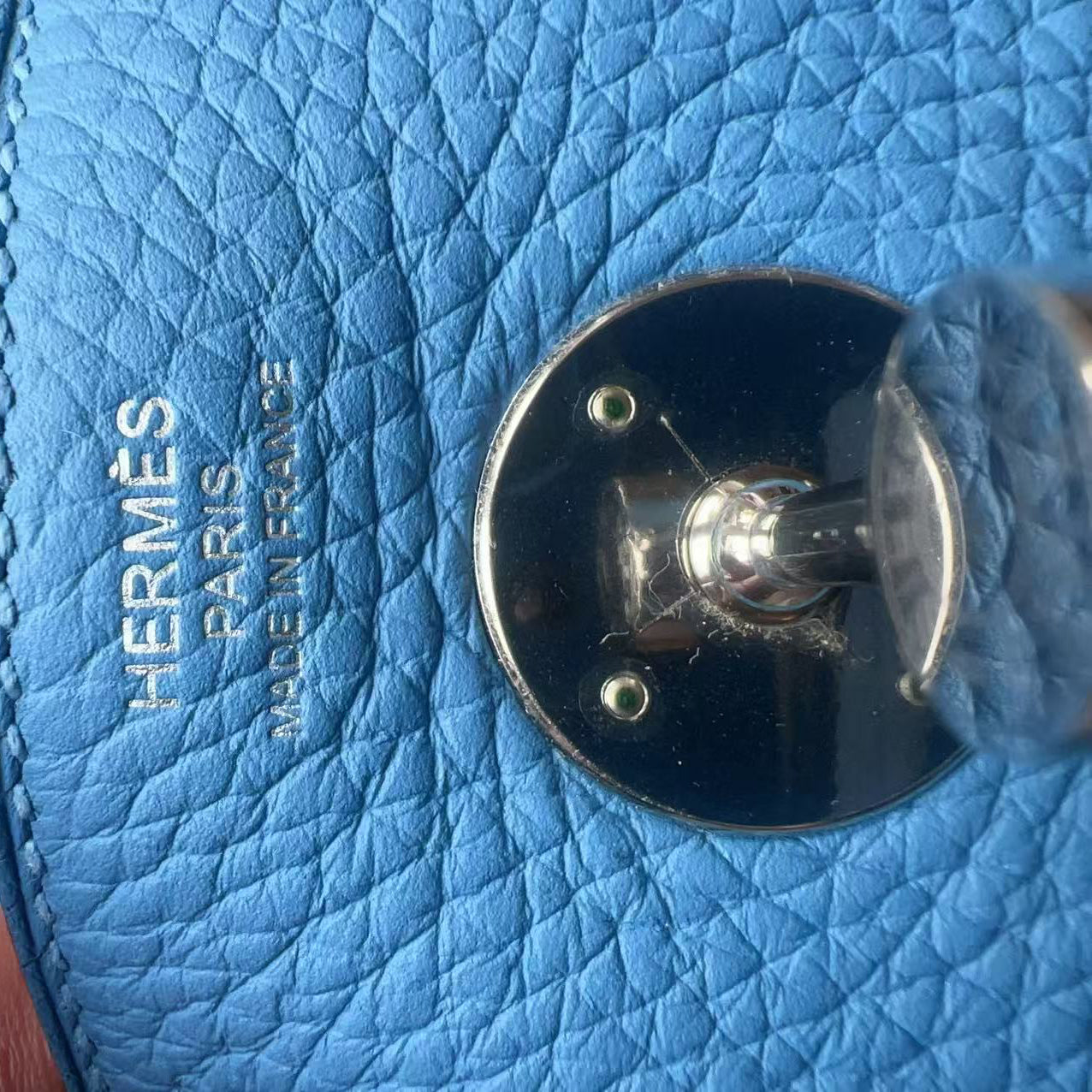Close-up of a light blue textured leather bag with silver-tone hardware and embossed HERMES PARIS MADE IN FRANCE text, held by a hand.