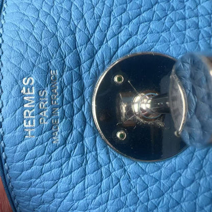 Close-up of a light blue textured leather bag with silver-tone hardware and embossed HERMES PARIS MADE IN FRANCE text, held by a hand.