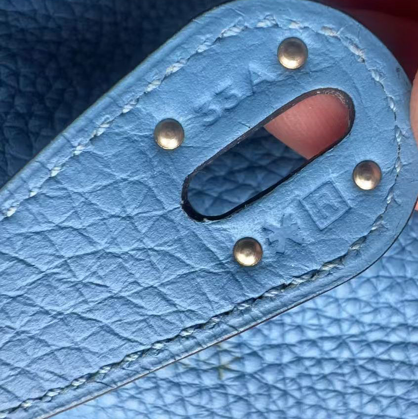 Close-up of a light blue textured leather strap with metal rivets and a cutout, held by fingers to show detail.