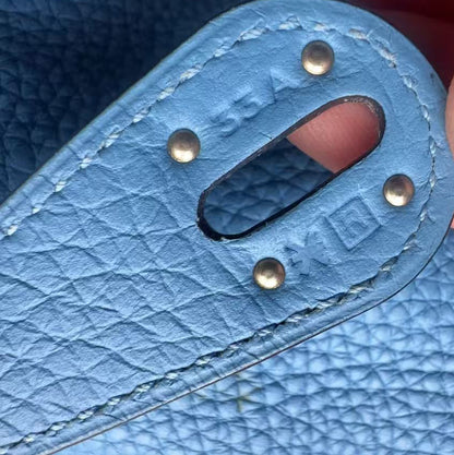 Close-up of a light blue textured leather strap with metal rivets and a cutout, held by fingers to show detail.