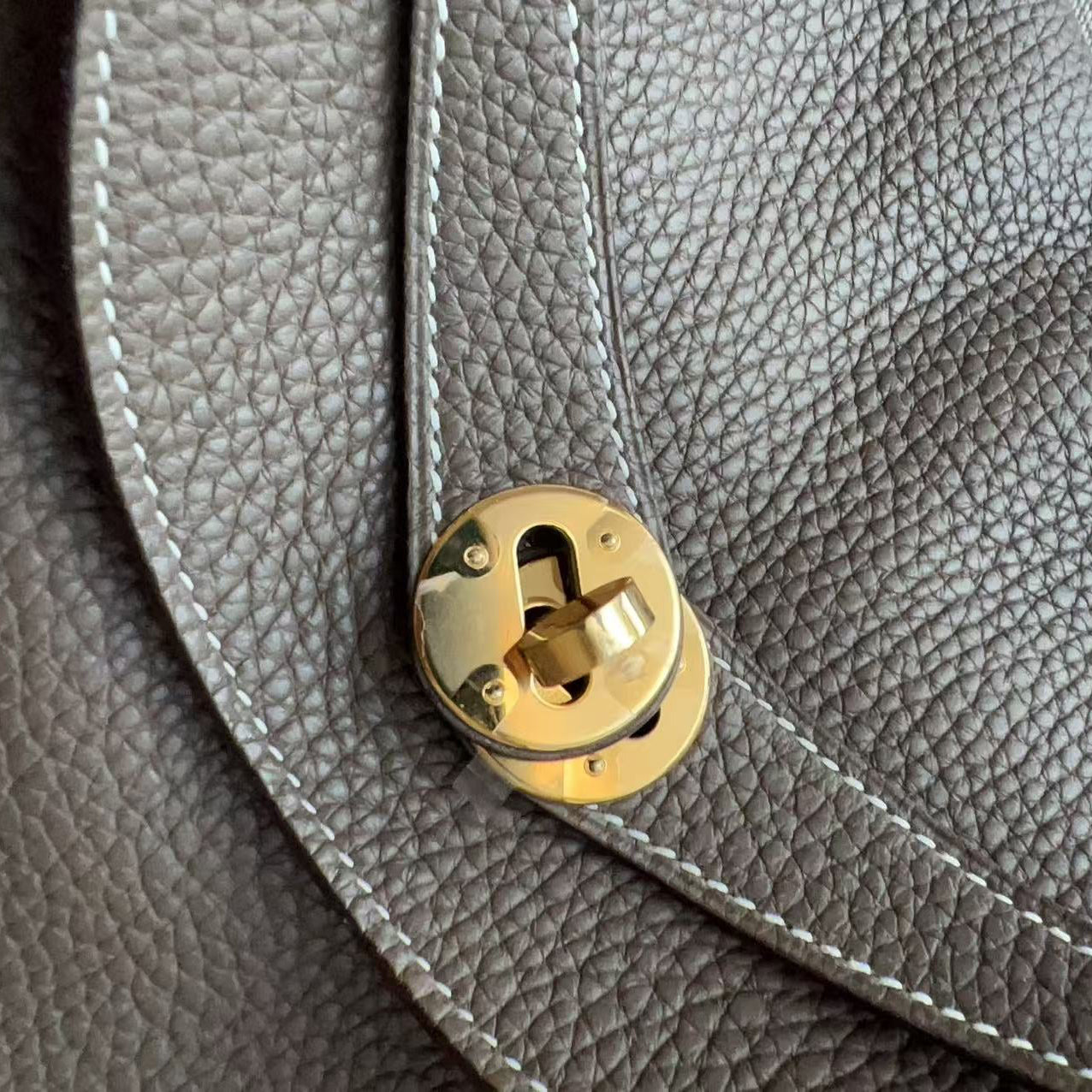 Close-up of a taupe pebbled leather bag with white stitching and a gold-tone metal clasp.