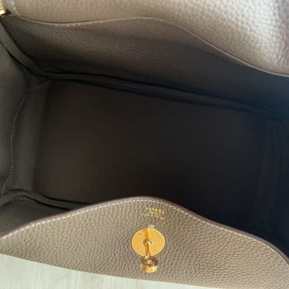 Close-up view of the interior of a taupe pebbled leather handbag, showing the dark lining, a zippered pocket on the left with gold-tone zipper, and a gold-tone turn-lock closure on the front flap.