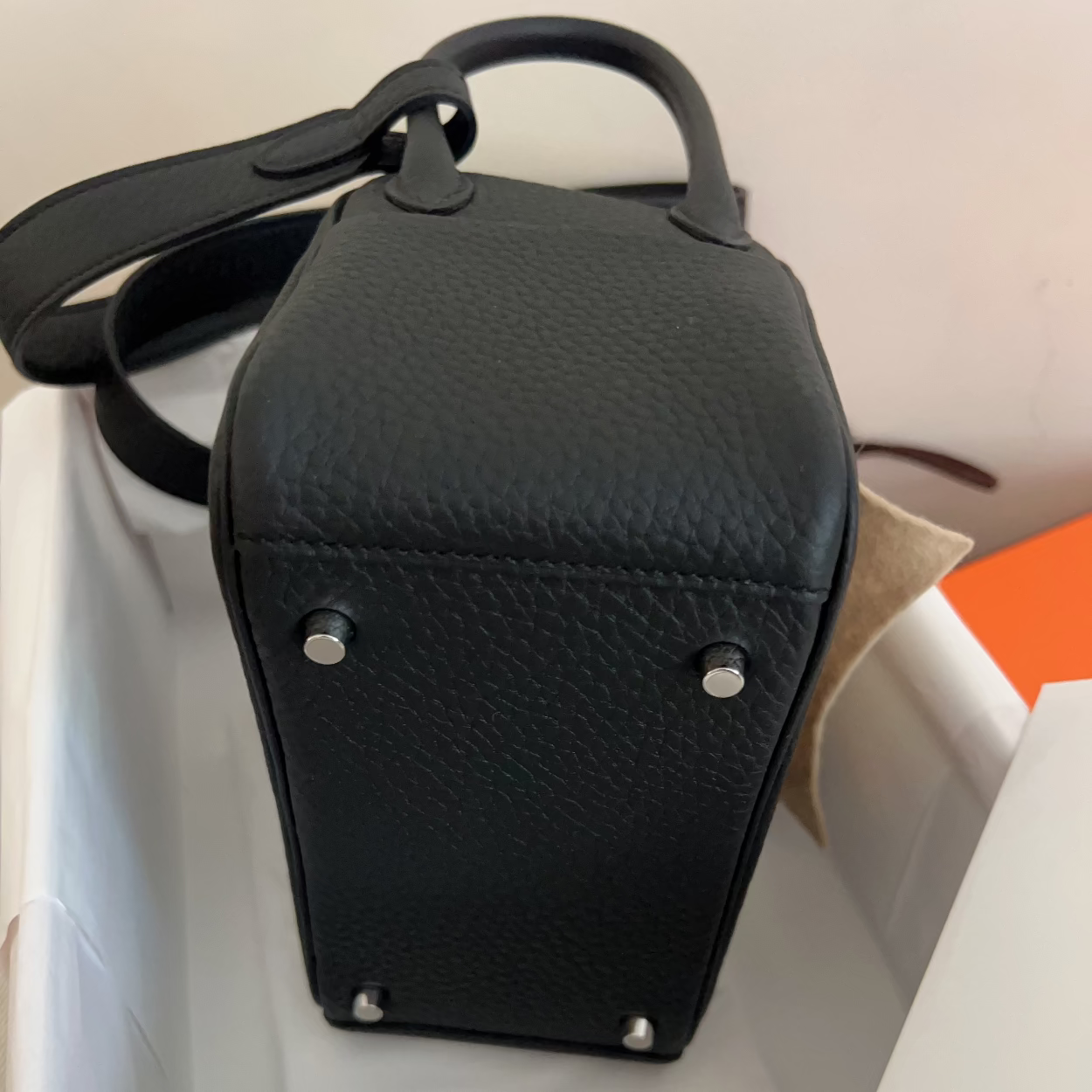 A black pebbled leather handbag with silver-tone studs, shown from the bottom corner inside a white box with white tissue paper.
