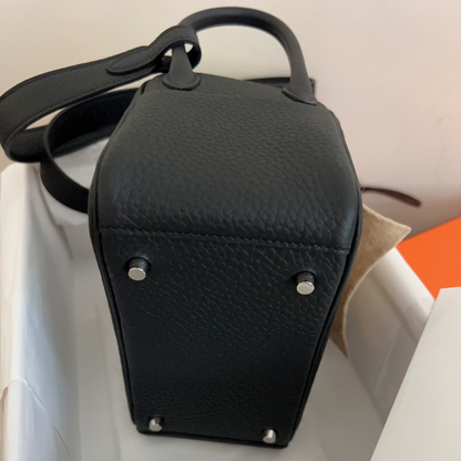 A black pebbled leather handbag with silver-tone studs, shown from the bottom corner inside a white box with white tissue paper.
