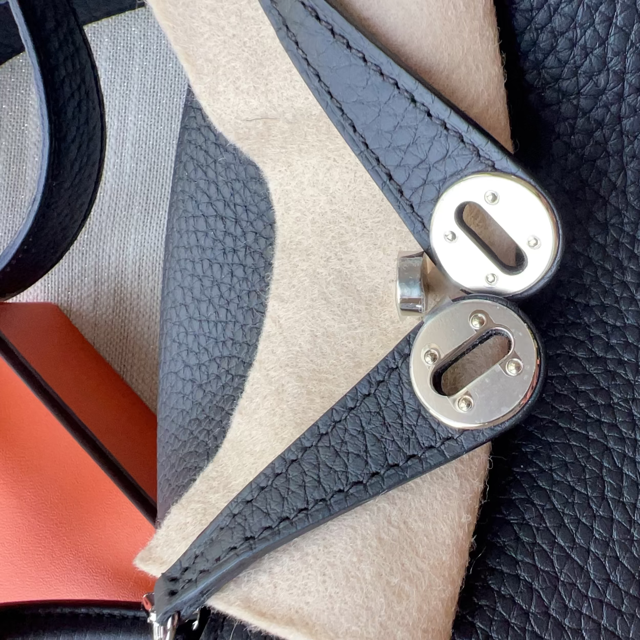 Close-up of a luxury handbag featuring textured black leather, a beige felt panel, and silver-tone metal hardware.