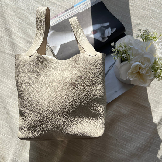 Beige handbag on a textured surface with a magazine and flowers in the background