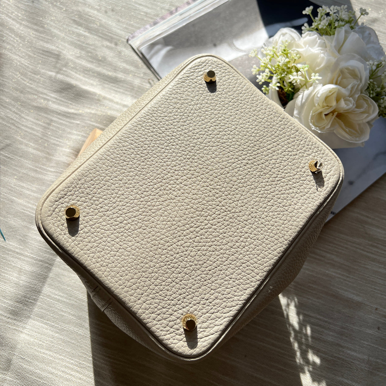 Beige leather pouch on a wooden surface with flowers and books in the background