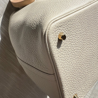 Close-up of a beige textured bag with a wooden wheel on a light gray surface.