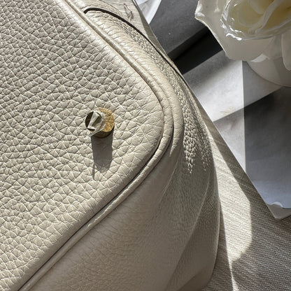 Close-up of a beige leather handbag with a floral arrangement in the background