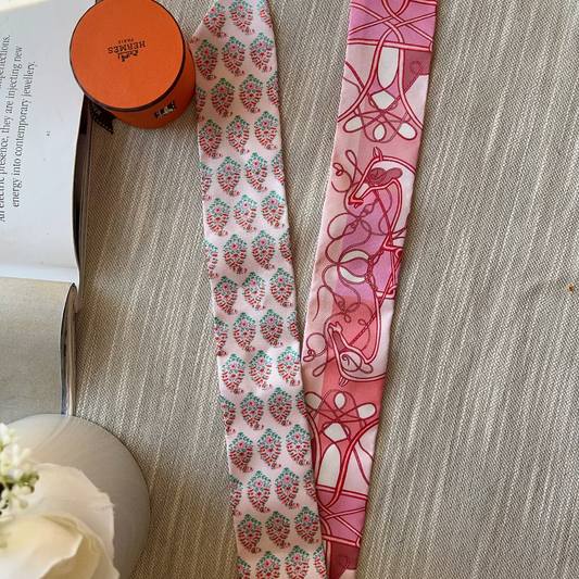 Two patterned ribbons on a textured surface with a book and small container in the background.