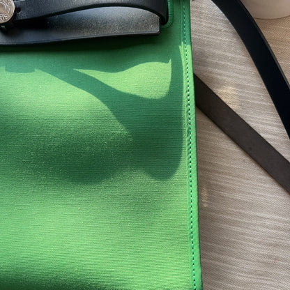 Green clutch bag with black strap on a wooden surface