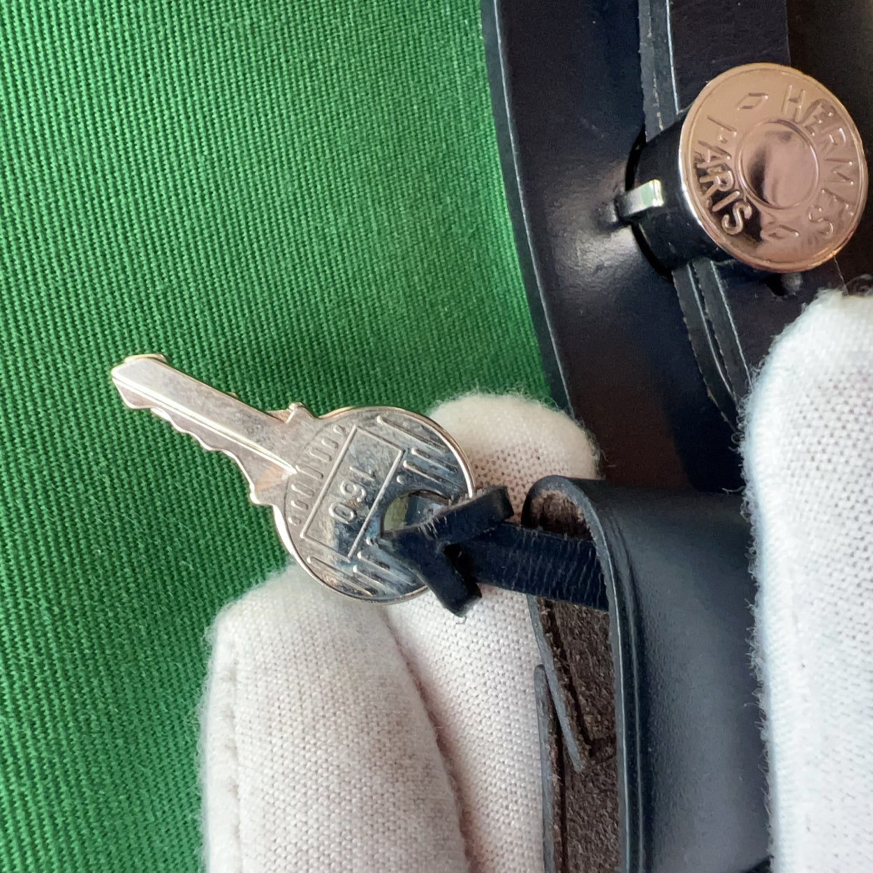 Close-up of a key and coin on a green surface with a white glove.