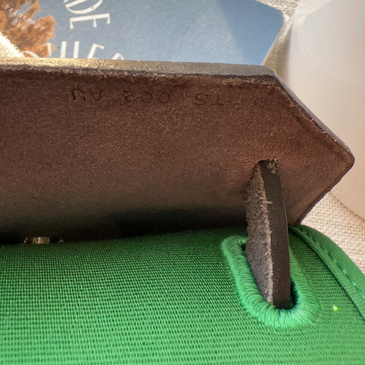 Close-up of a brown leather product with a visible brand name, placed on a green surface.