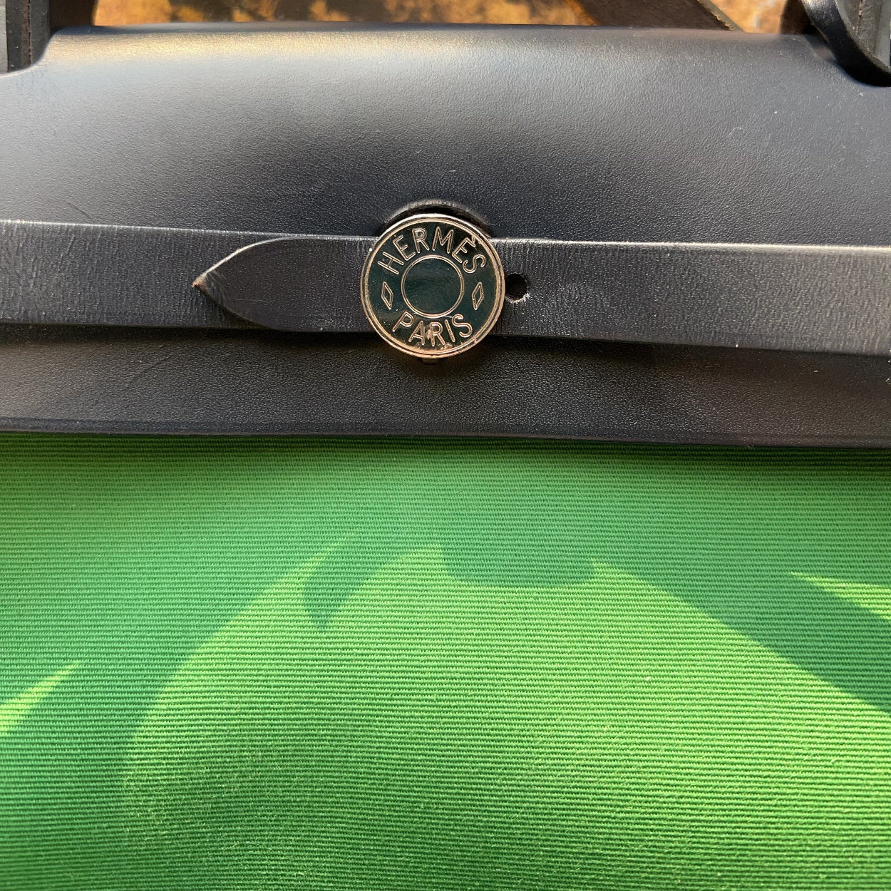 Close-up of a Hermès bag with a visible logo on a green surface.