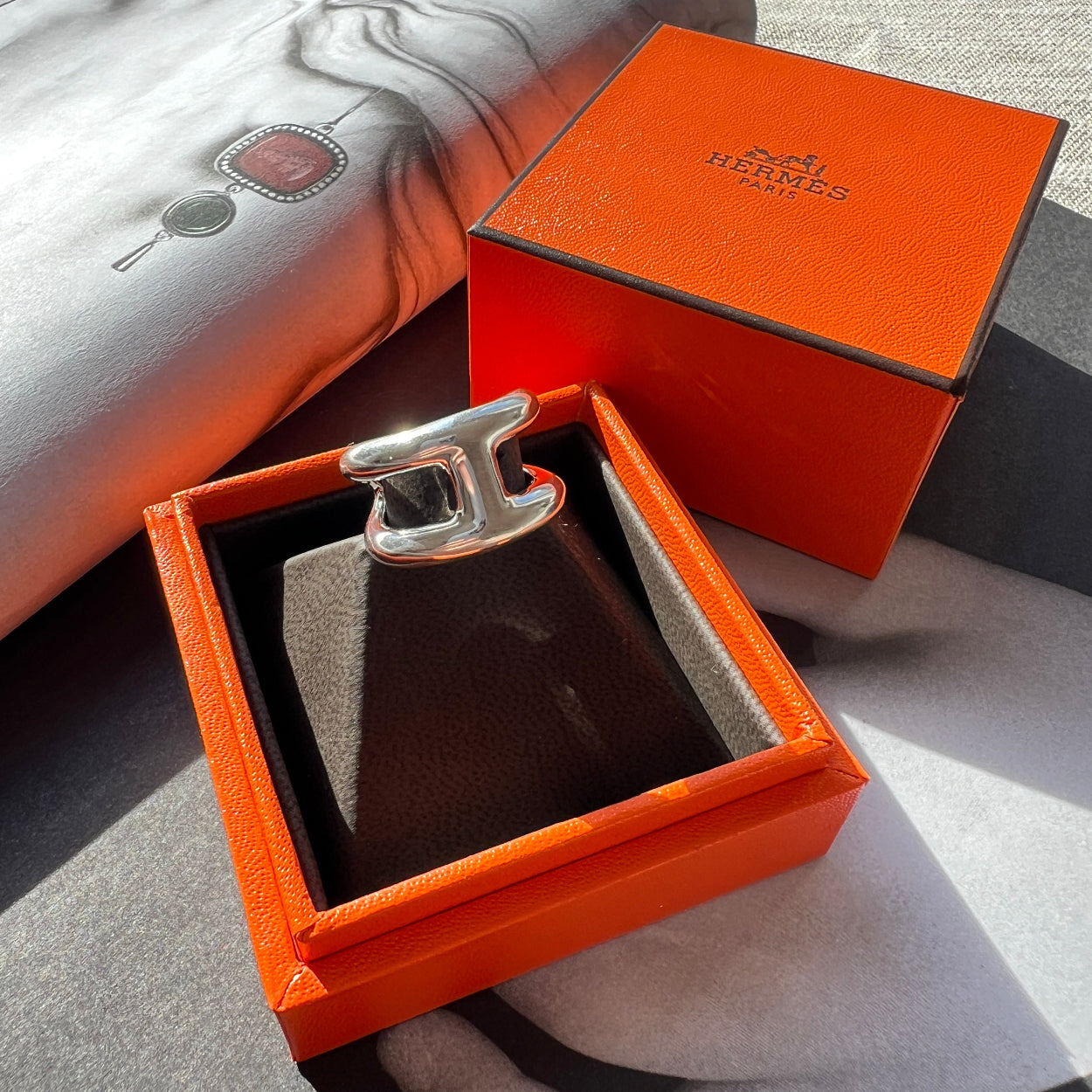Silver belt buckle in an open orange box on a textured surface