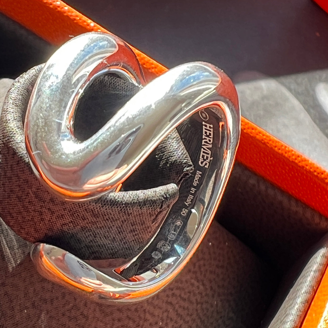 Silver Hermès belt buckle on a brown leather background