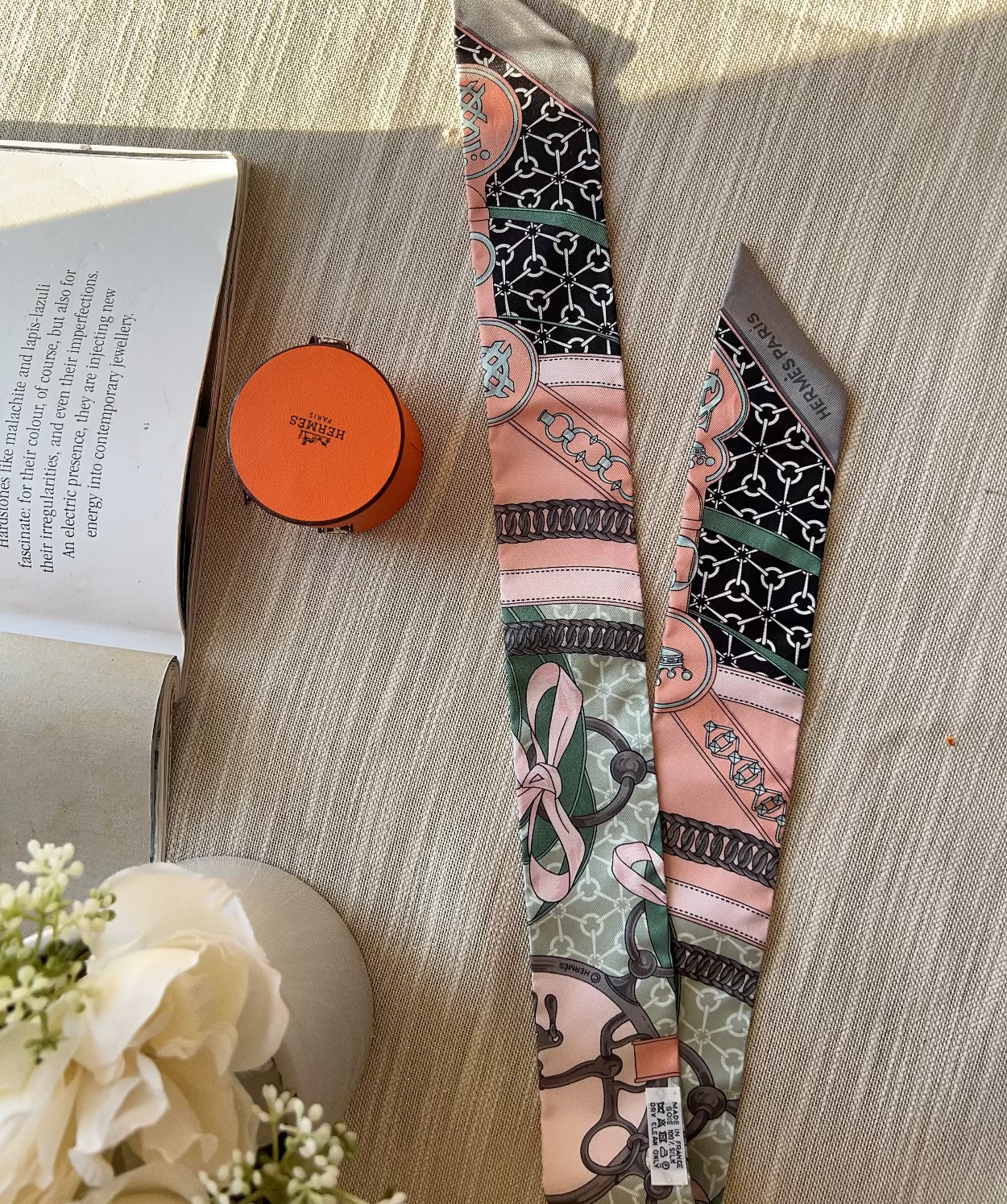 Patterned tie on a wooden surface with an open book and small round object nearby.