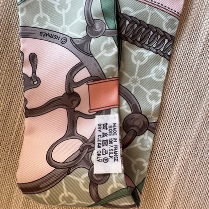 Hermes scarf with intricate design and brand label on a textured surface
