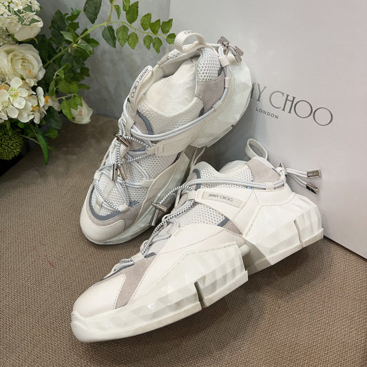 White high-top sneakers with gray accents next to a Yves Saint Laurent box on a brown surface.