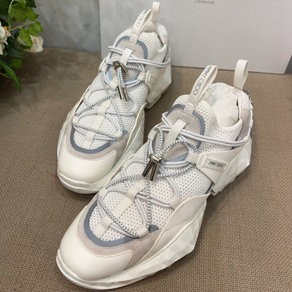 White sneakers with blue accents on a textured surface, with a Jimmy Choo box in the background.