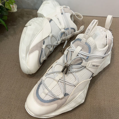 White and gray sneakers on a textured surface with 'Jimmy Choo' branding in the background.