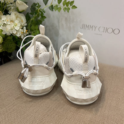 White sneakers with silver accents on a textured surface, with 'Jimmy Choo' branding in the background.