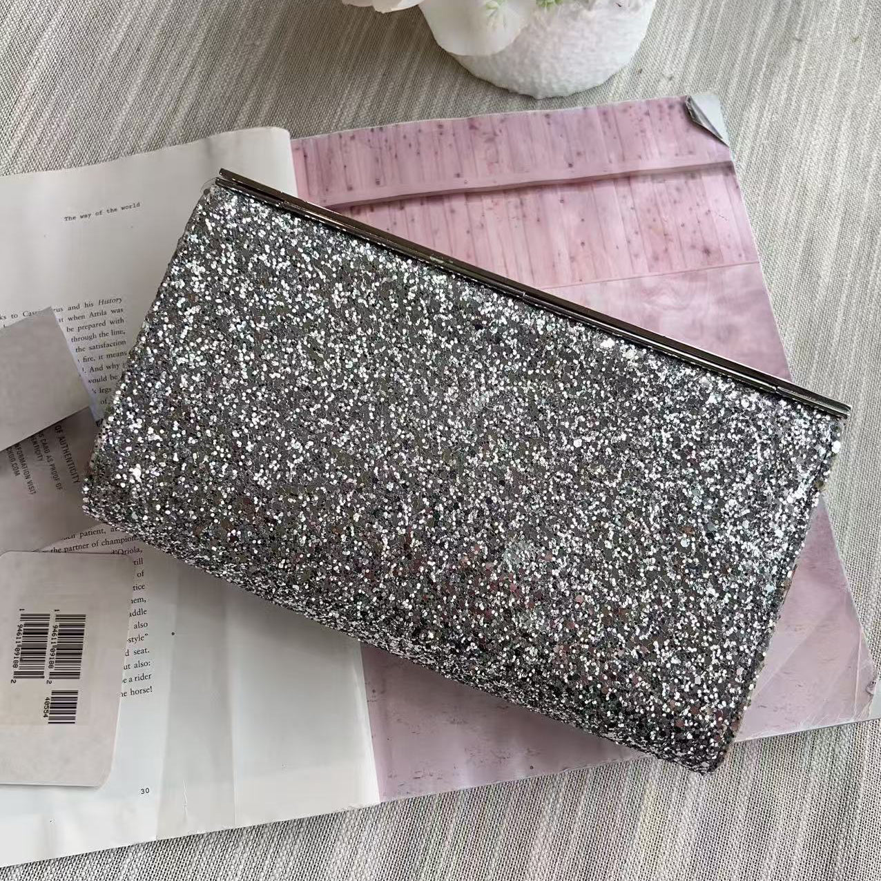 Silver glittery clutch bag on a pink surface with flowers in the background