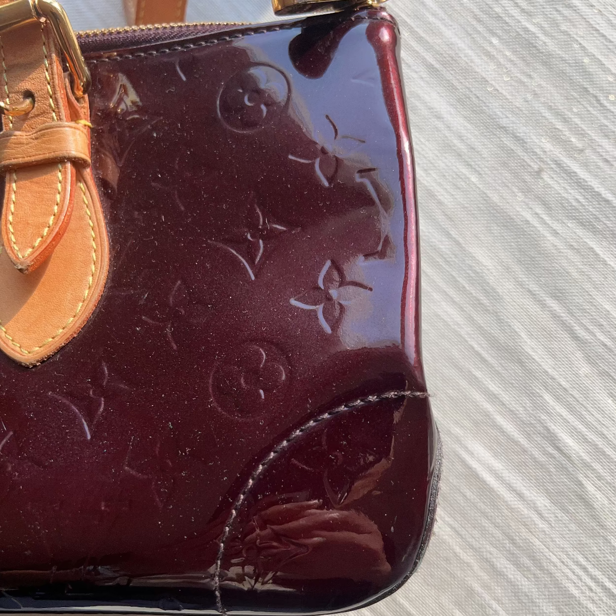 Maroon handbag with tan strap on a textured surface