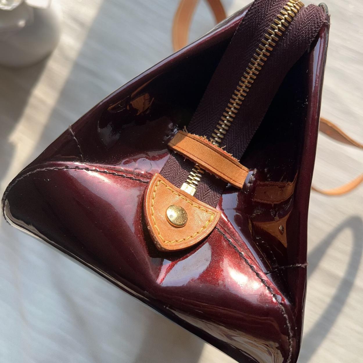 Triangular red patent leather wallet with brown accents on a light surface.