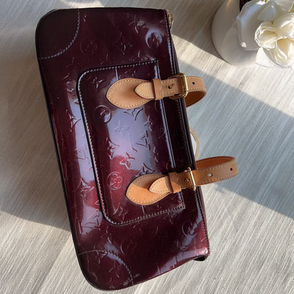 Maroon leather clutch with gold accents on a light wooden surface