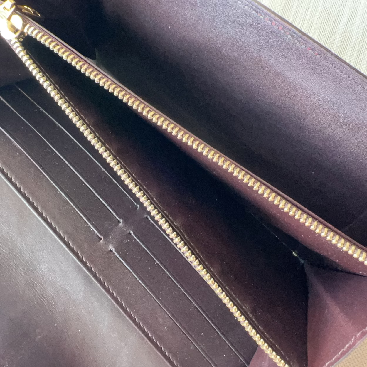 Close-up of a dark brown leather wallet with gold zipper on a light background