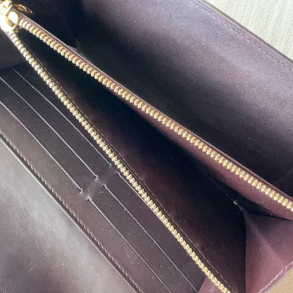 Close-up of a dark brown leather wallet with gold zipper on a light background