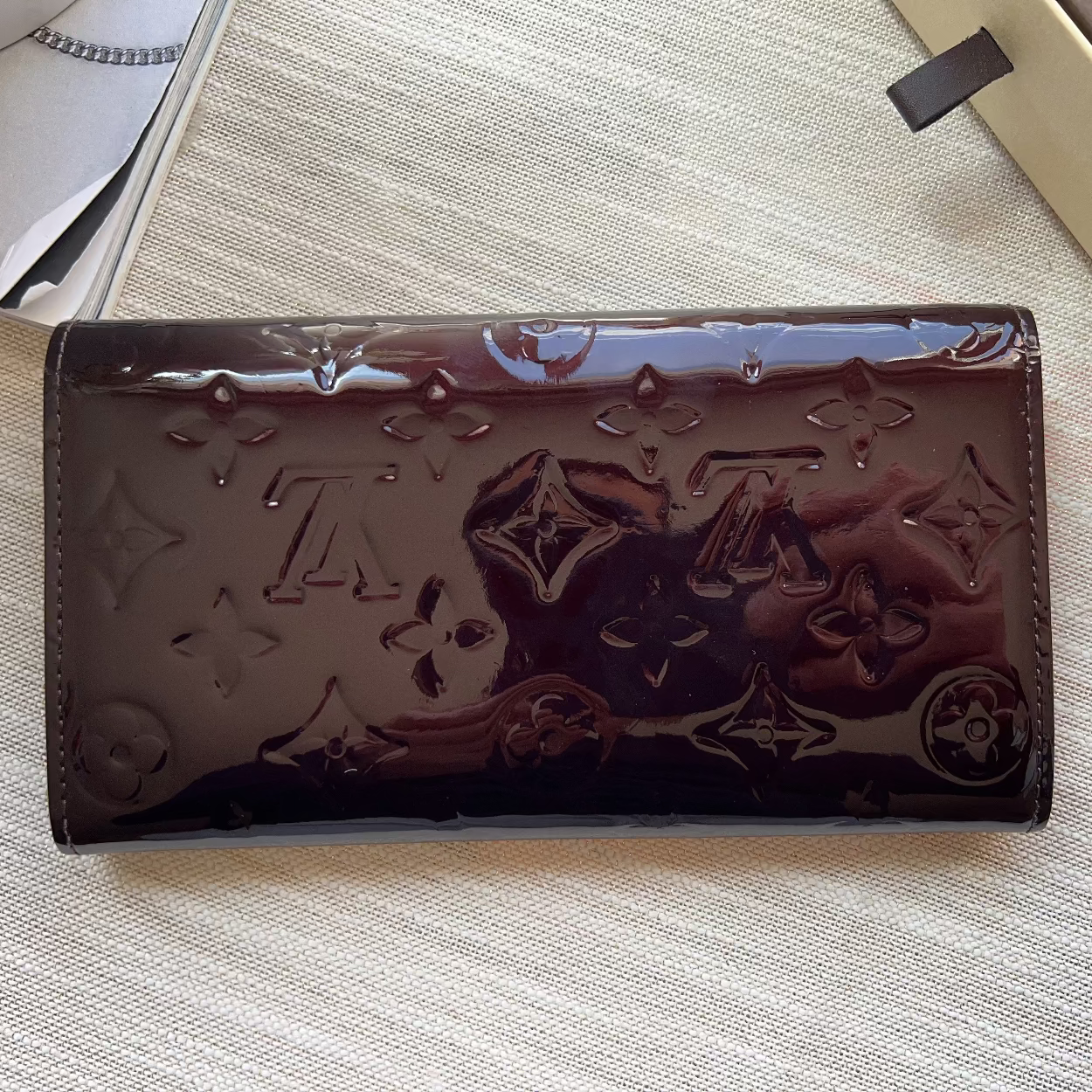 Burgundy patent leather wallet with brand logo on a light textured surface
