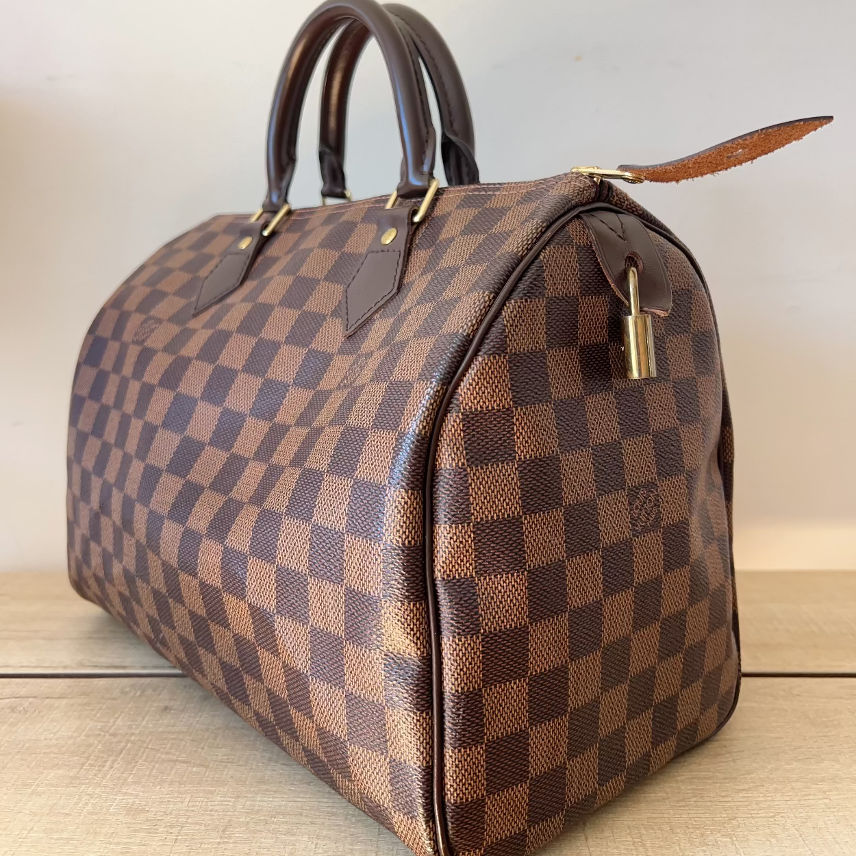 Brown checkered handbag with gold lock on a light wooden surface