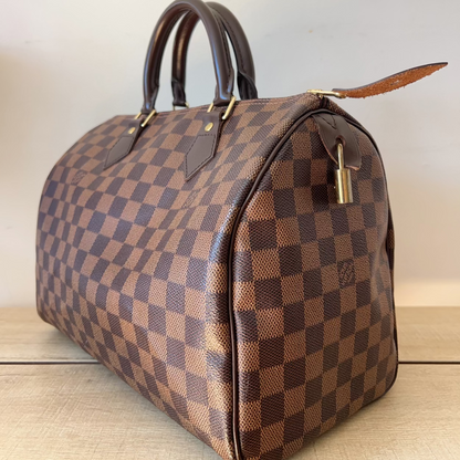 Brown checkered handbag with gold lock on a light wooden surface