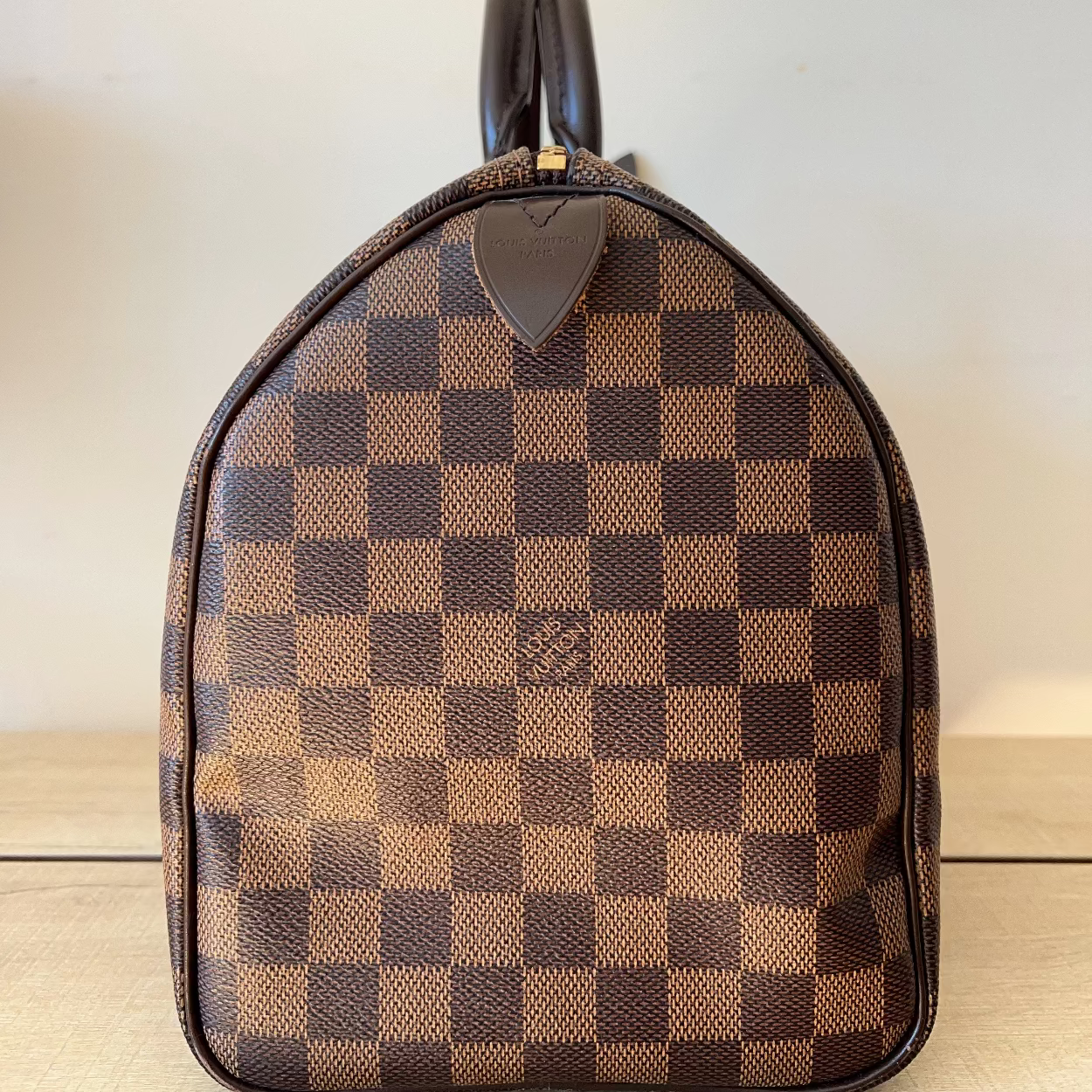 Brown checkered handbag on a wooden surface with a light background