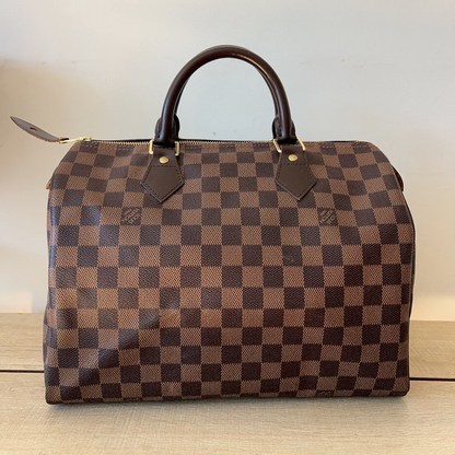 Brown checkered handbag with gold accents on a light background
