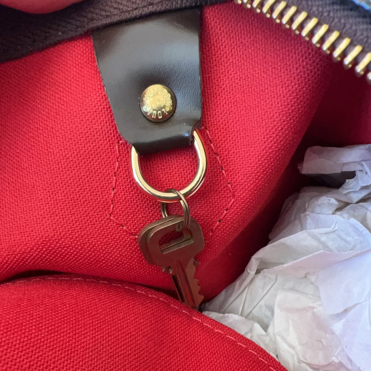Close-up of a red bag with a gold zipper pull and keychain.