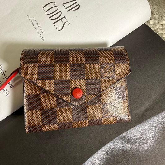 Brown checkered wallet with red button on a dark surface