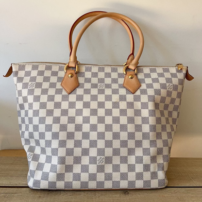 Checkered handbag with brown handles and trim on a wooden surface.