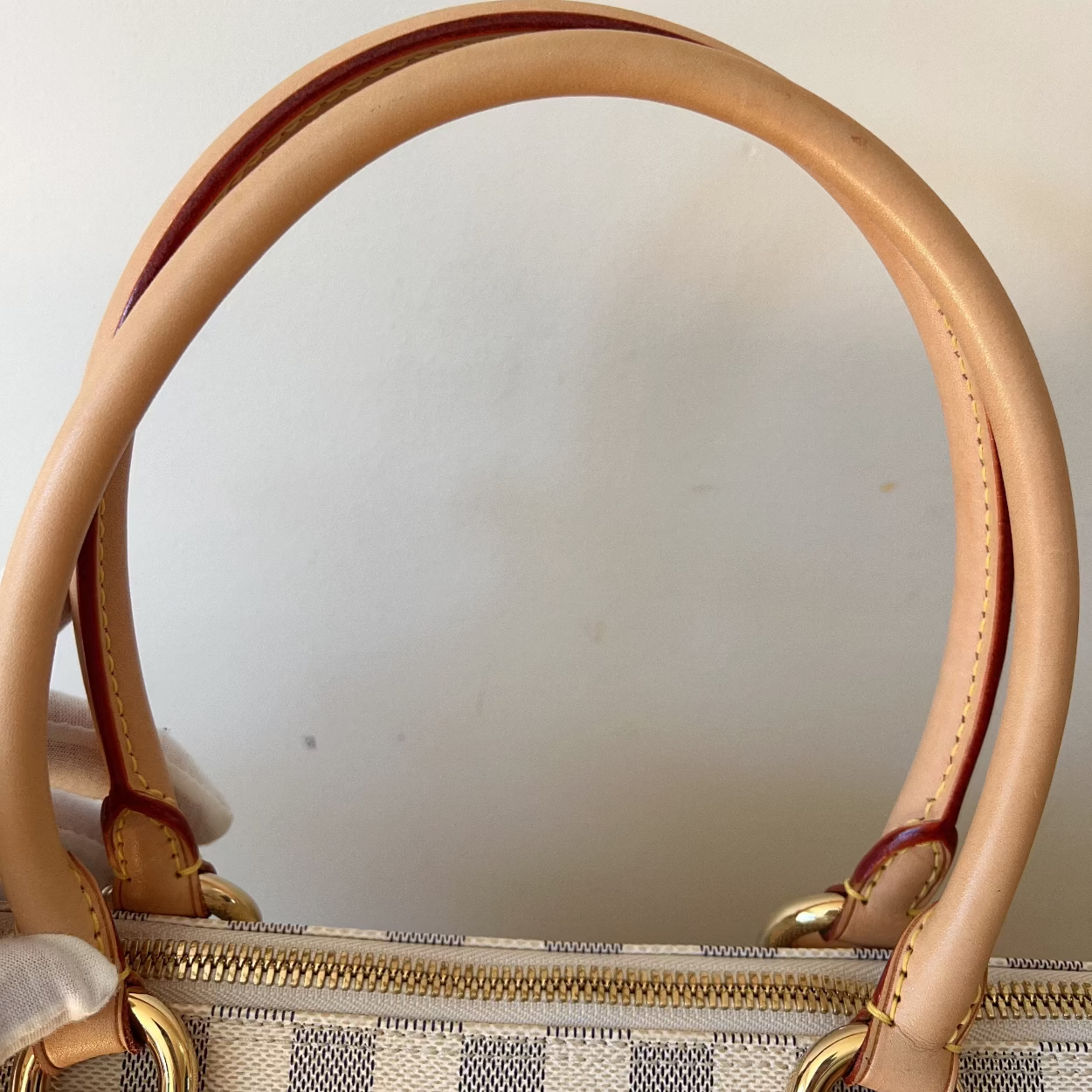 Close-up of a handbag with checkered pattern and gold accents on a white background