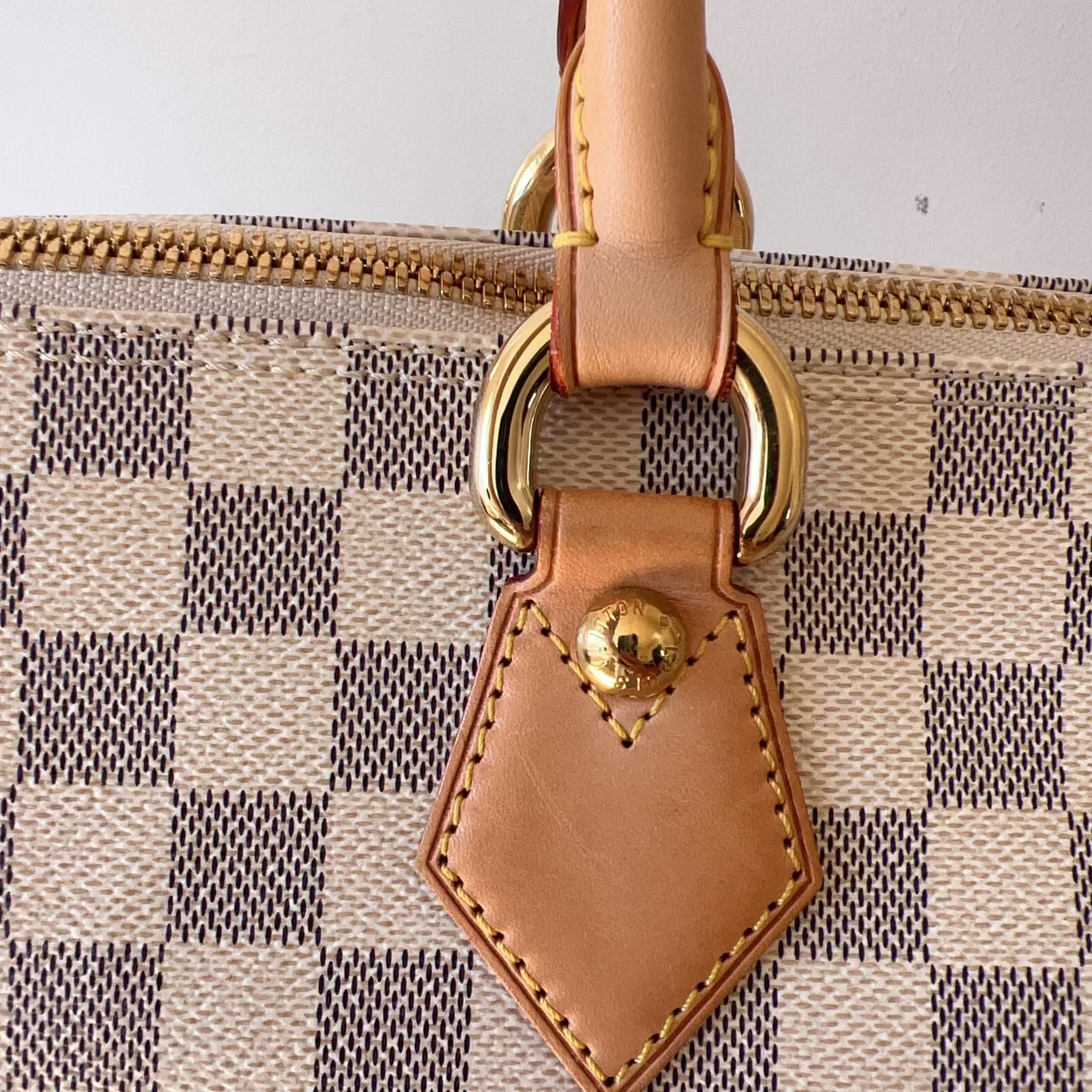 Close-up of a patterned handbag with a brown leather tag and gold ring.