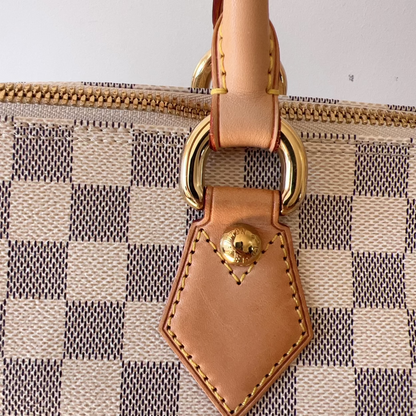 Close-up of a patterned handbag with a brown leather tag and gold ring.