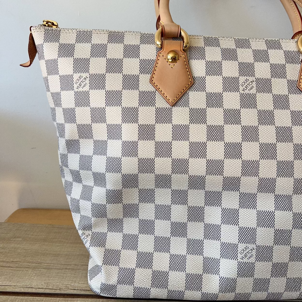 Checkered handbag with brown leather handles and zipper on a wooden surface.
