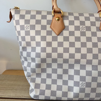 Checkered handbag with brown leather handles and zipper on a wooden surface.