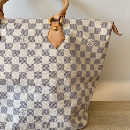 Checkered handbag with brown leather handle and strap on a wooden surface.