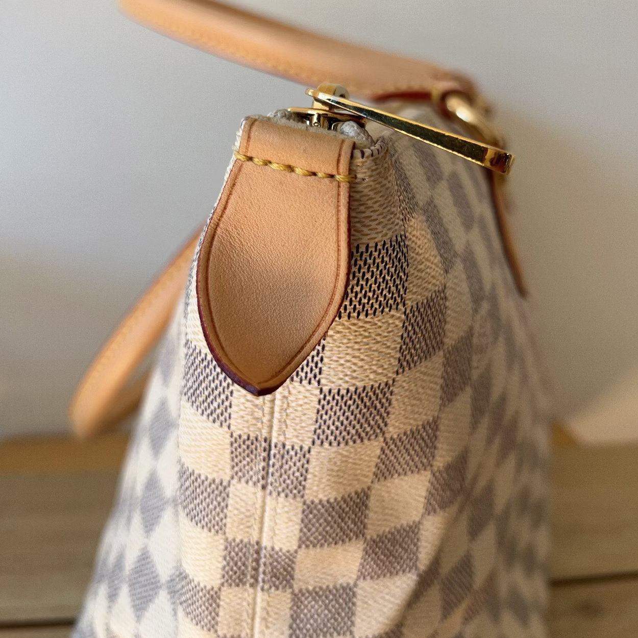 Close-up of a checkered handbag with a tan handle on a wooden surface.