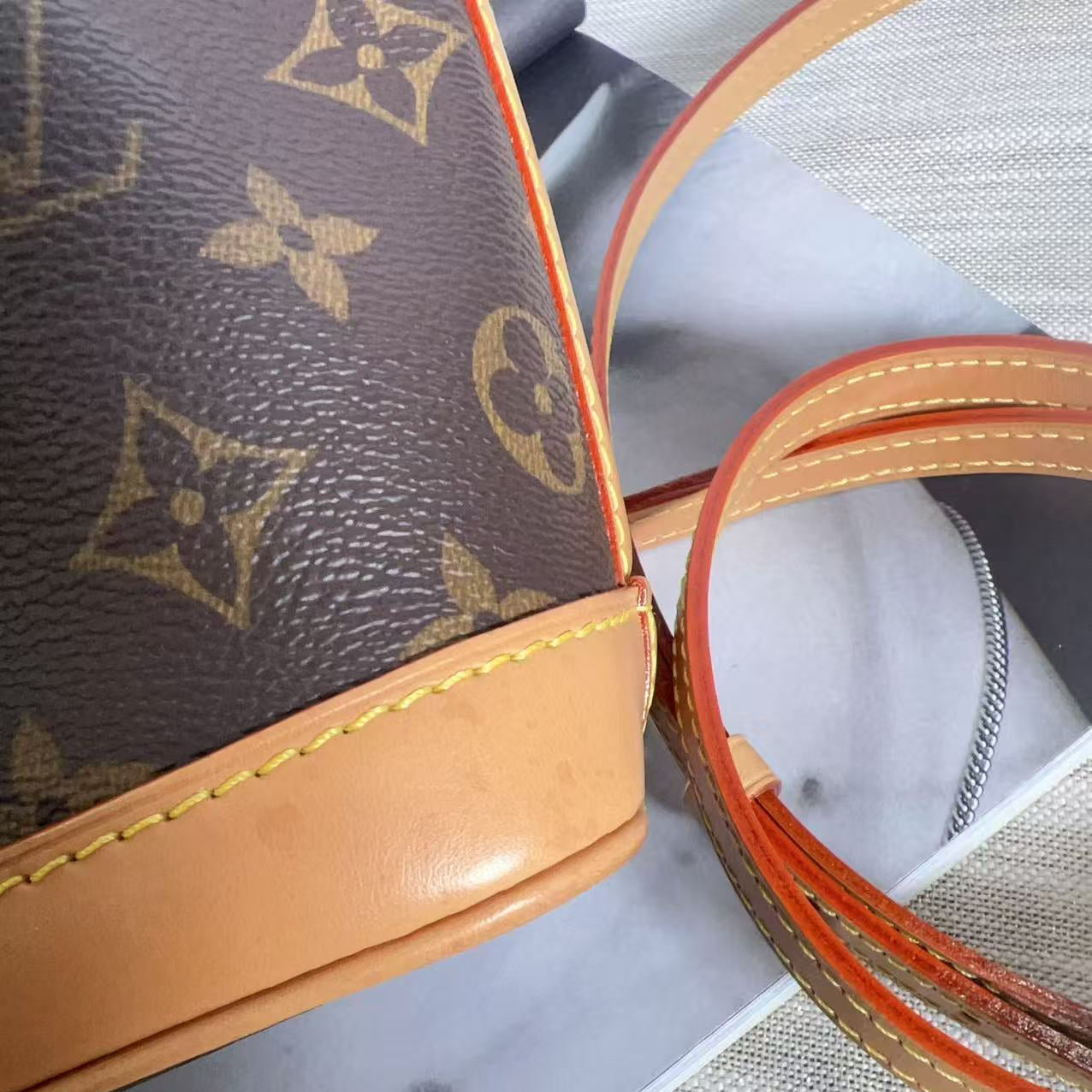 Close-up of a brown leather handbag with orange stitching on a textured surface.
