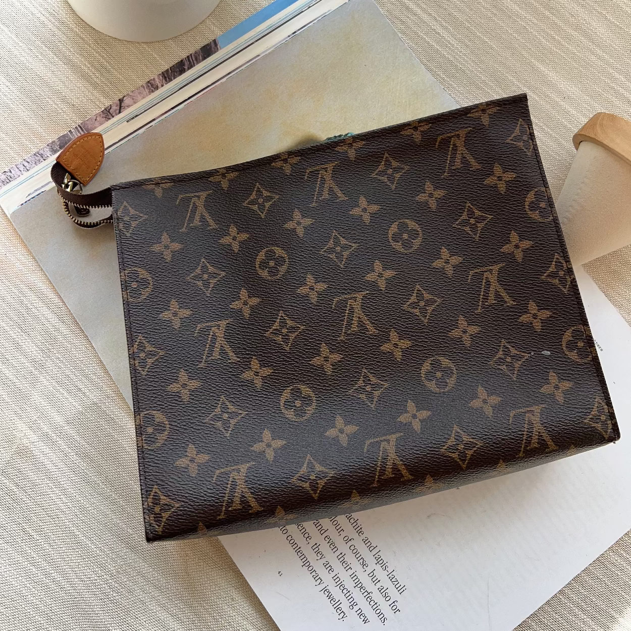 Louis Vuitton patterned notebook on an open book with flowers and a candle in the background