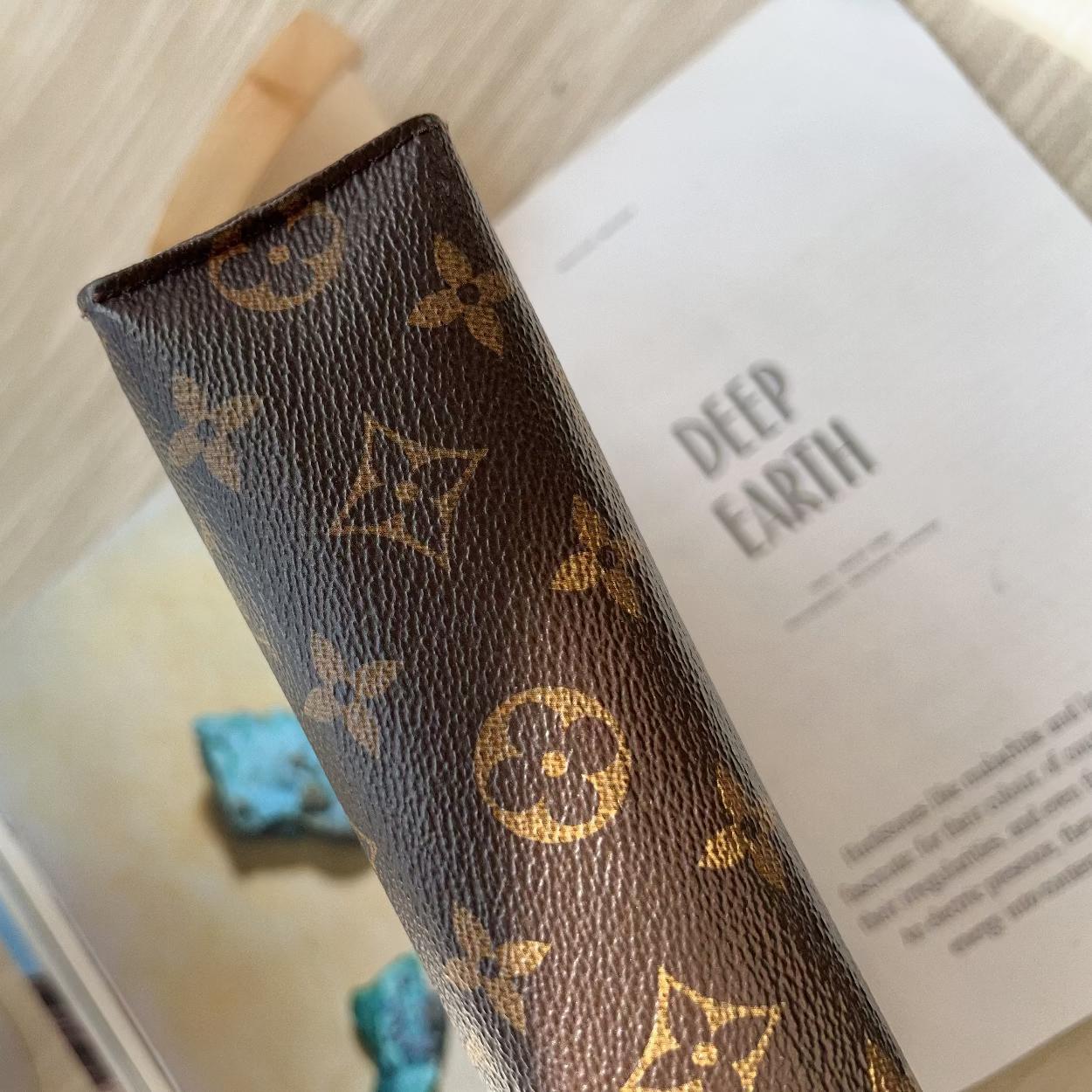 Brown leather wallet with gold monogram pattern on a book titled 'Deep Earth'.